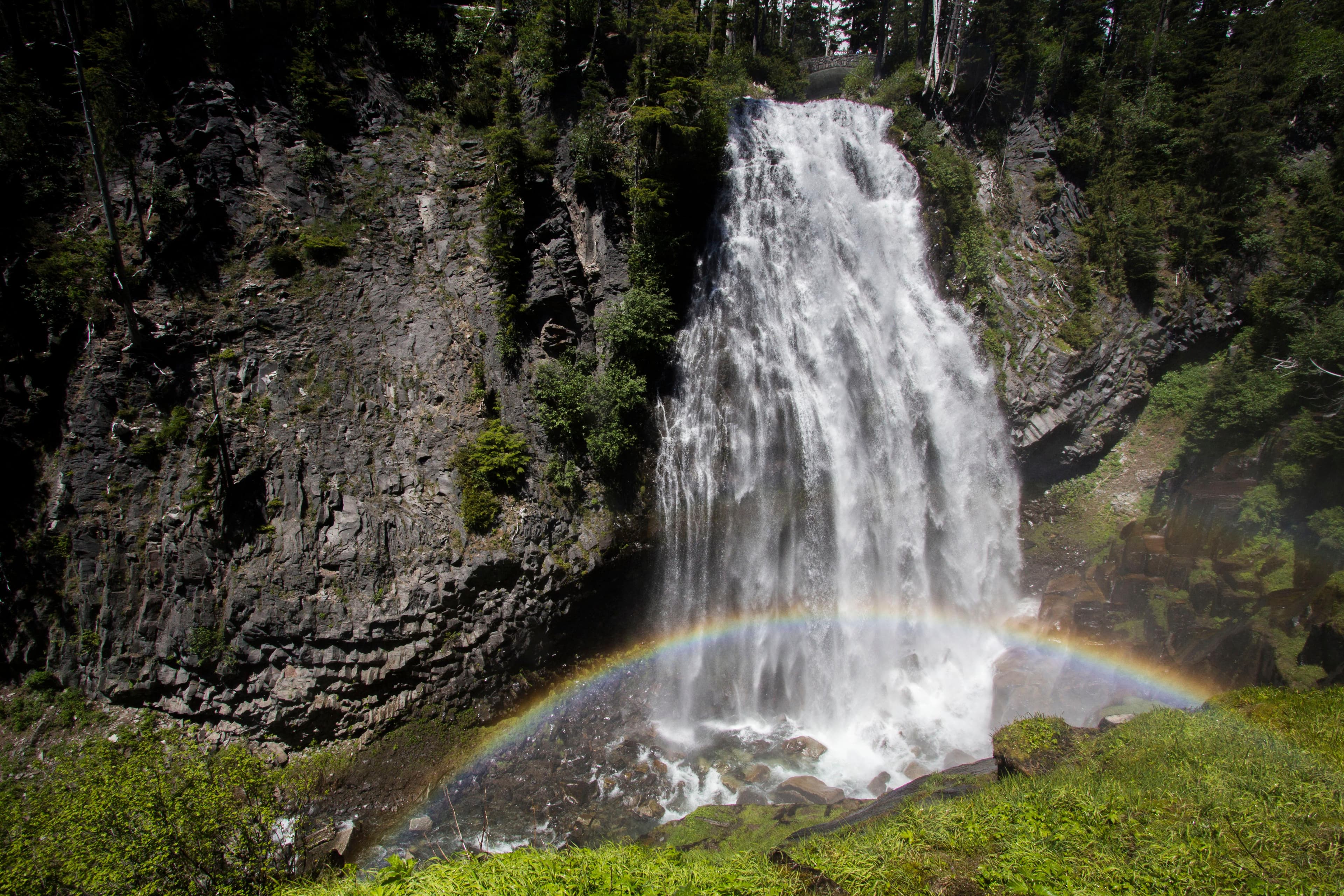 A fan-shaped waterfall cascades over lava cliffs with a rainbow in its mist.
